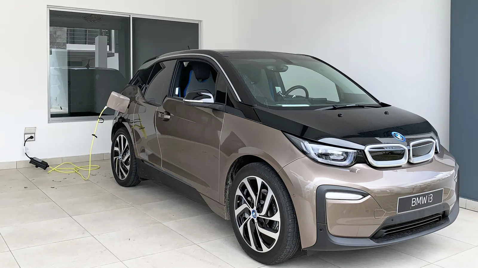 An electric car parked indoors, charging from a standard 120-volt wall outlet with a portable cord
