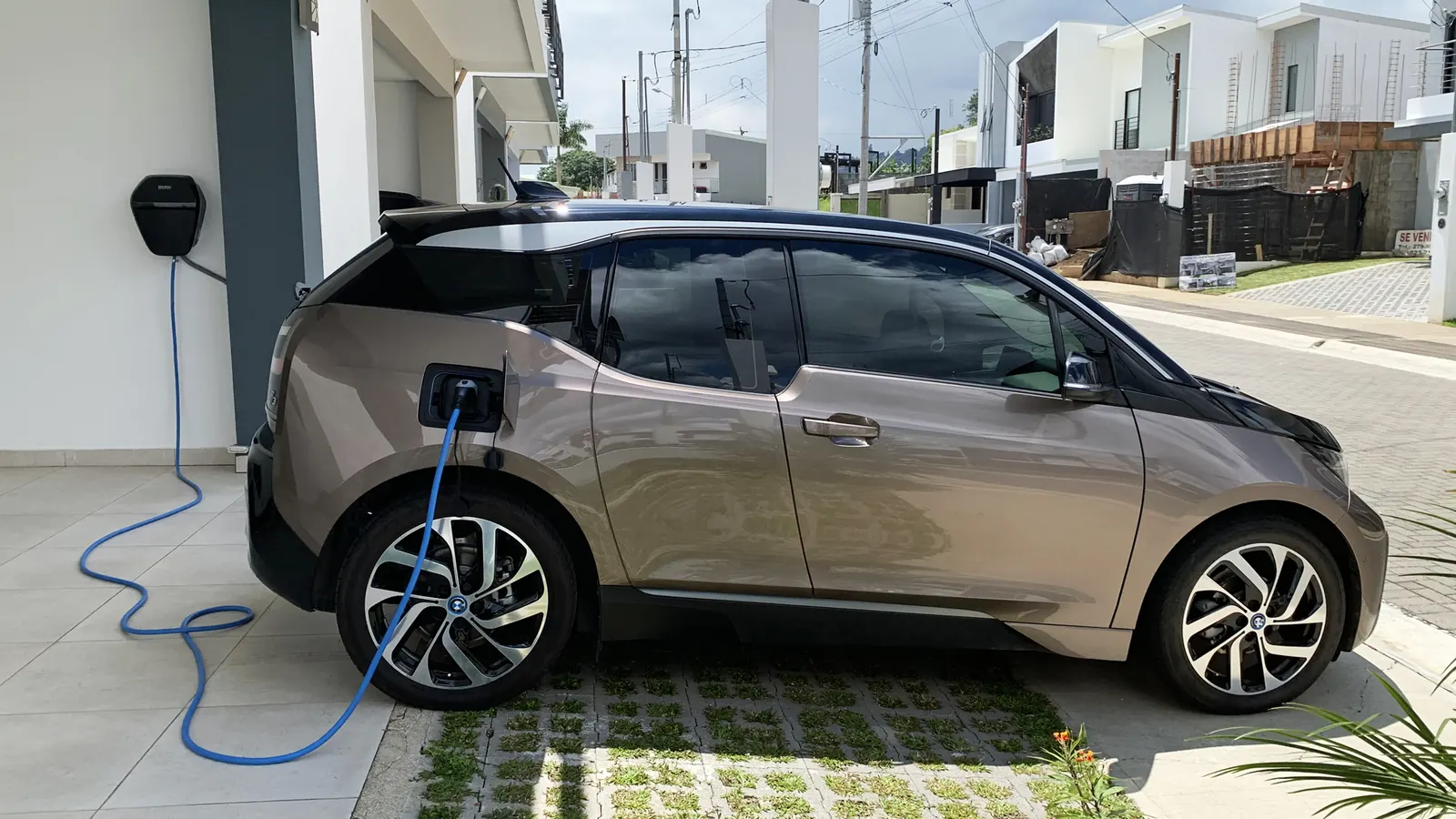 An electric car in a driveway, plugged into a wall-mounted Level 2 charger