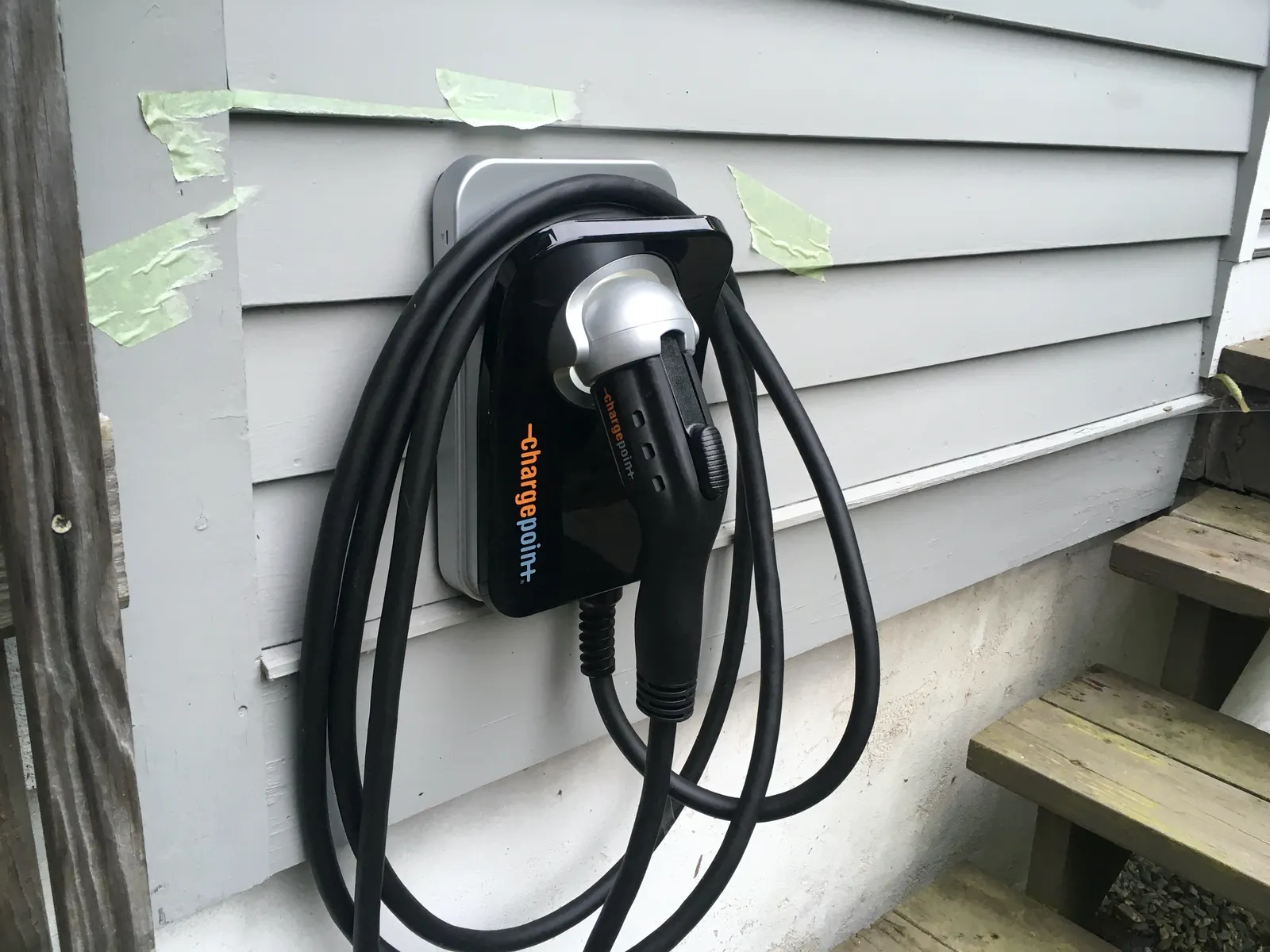 A Level 2 home EV charger mounted on a house's exterior siding with its cable coiled